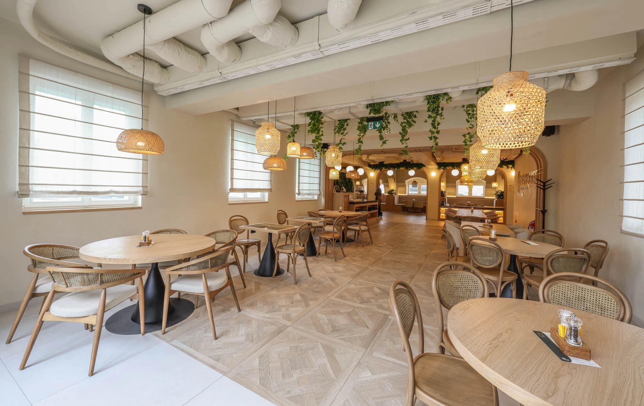 Modern dining room featuring wooden tables, woven chairs, and warm basket pendant lights throughout.