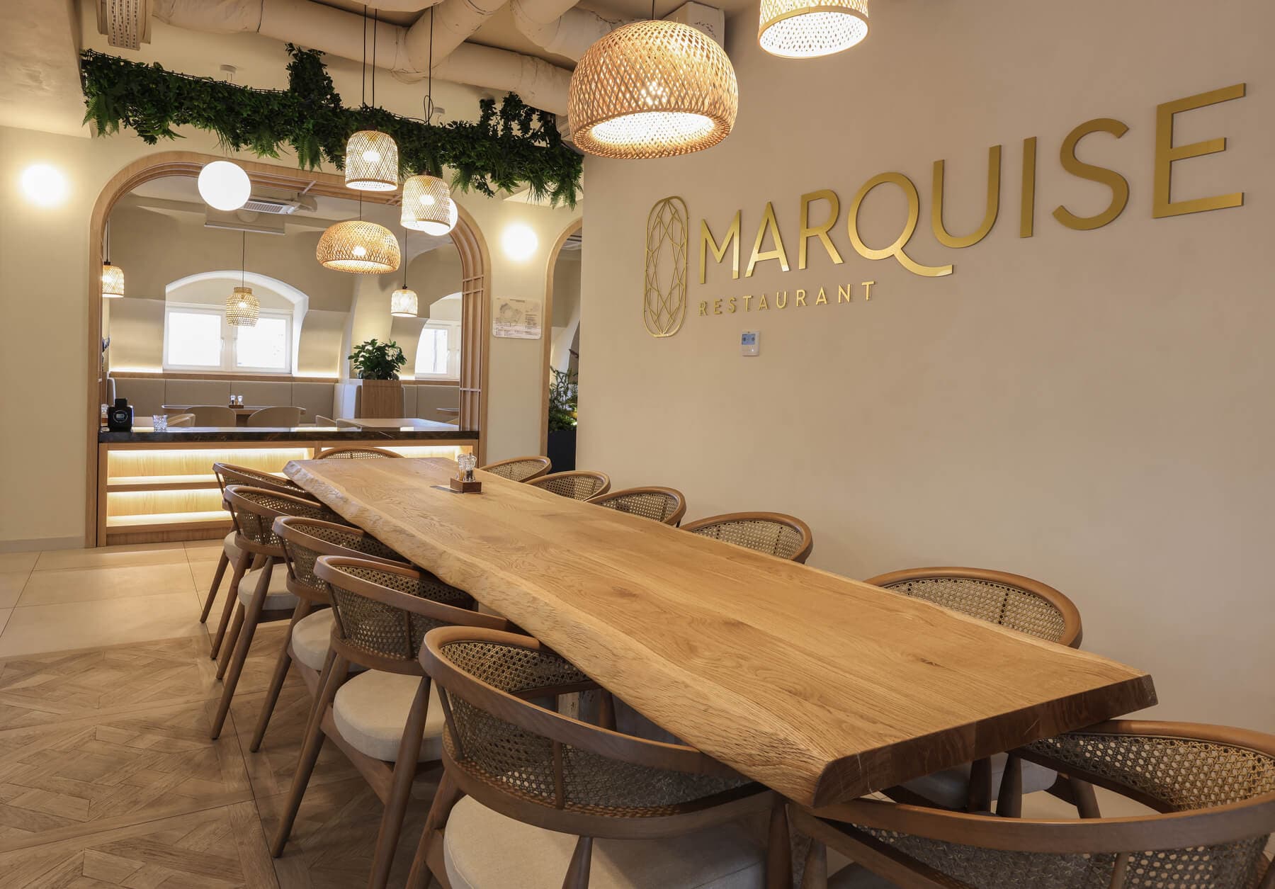 Long live-edge wooden table with woven chairs under stylish pendant lights at Marquise Restaurant.