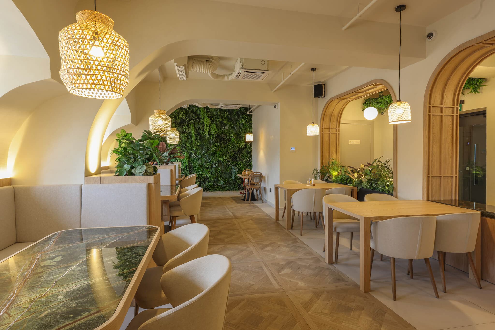 Modern restaurant interior with wooden tables, cream chairs, woven lamps, and a lush vertical garden.