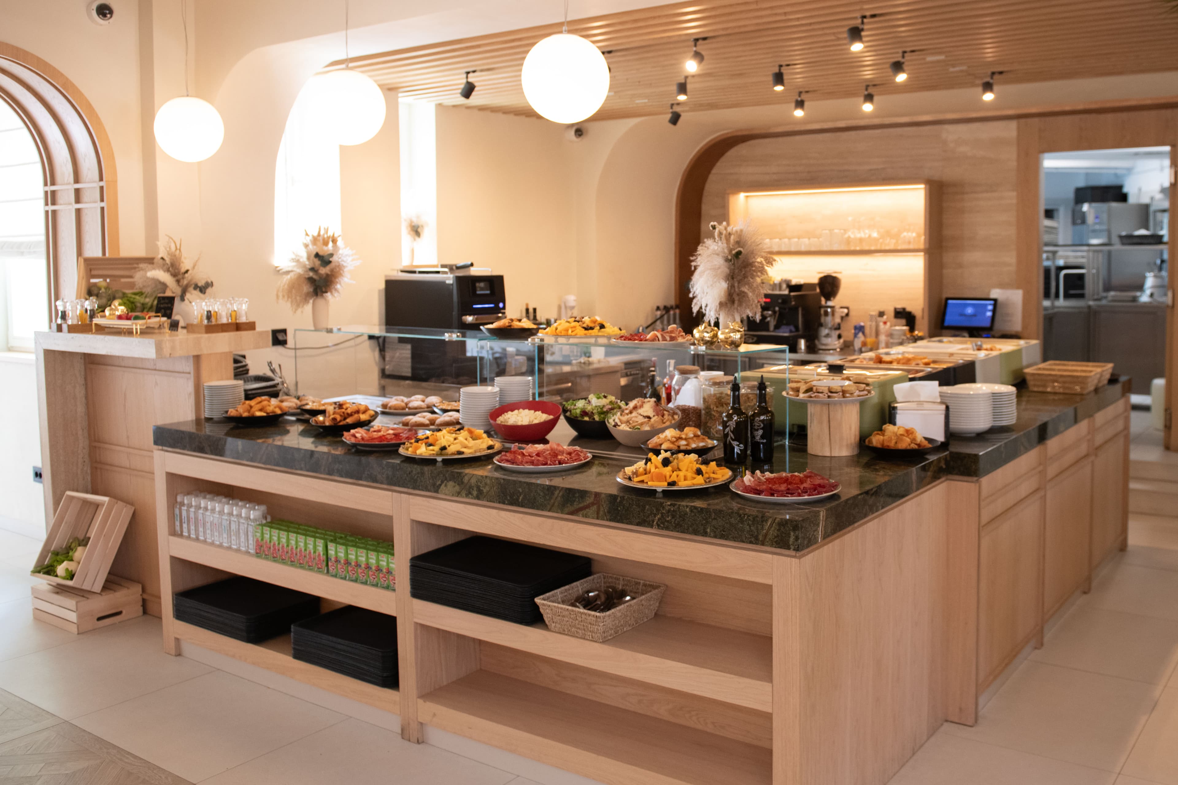 Breakfast buffet spread with meats, cheeses, fruits, and pastries on a modern wooden counter.