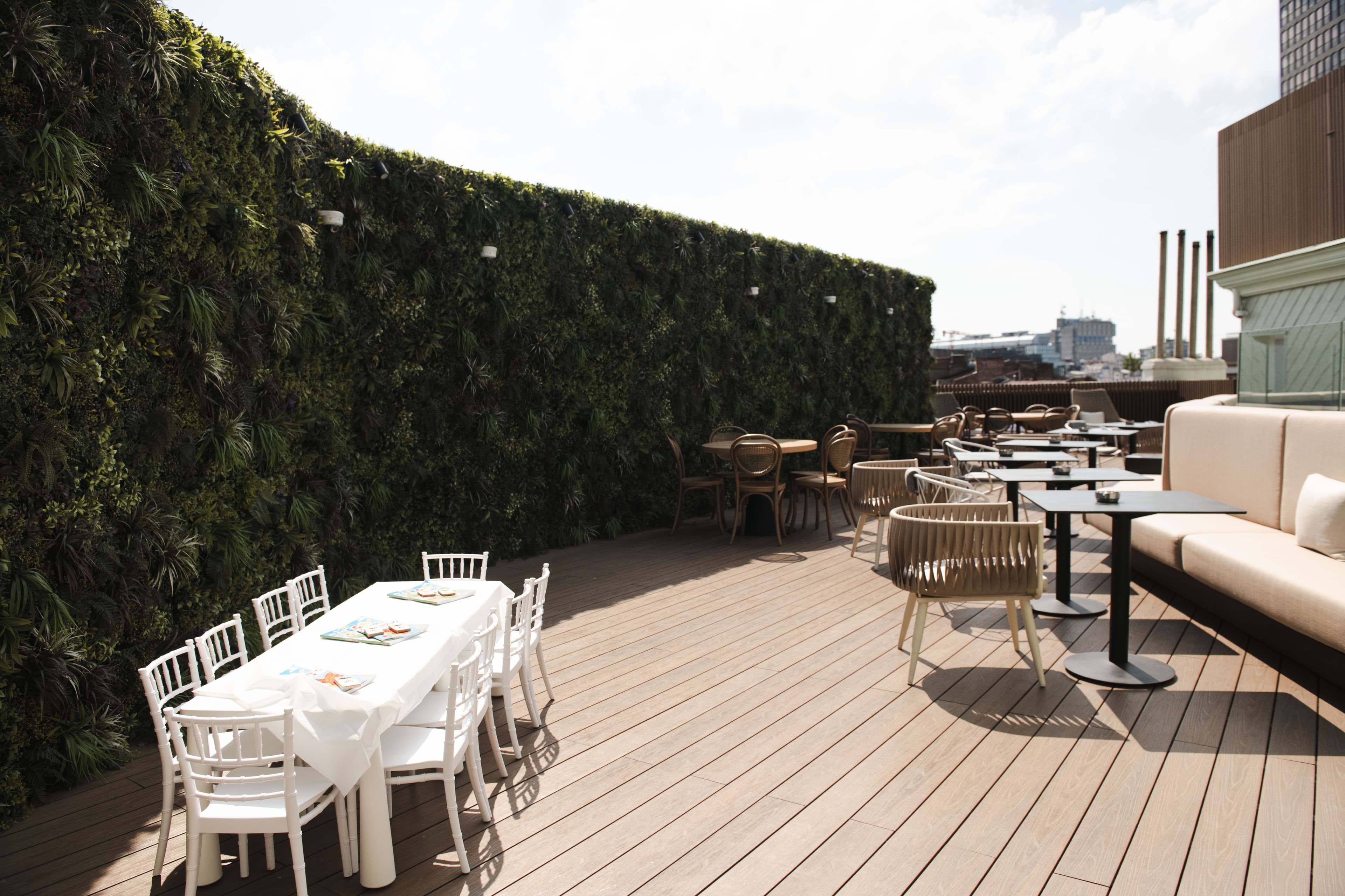 Rooftop terrace featuring a lush green wall, wooden decking, and various outdoor dining table sets.