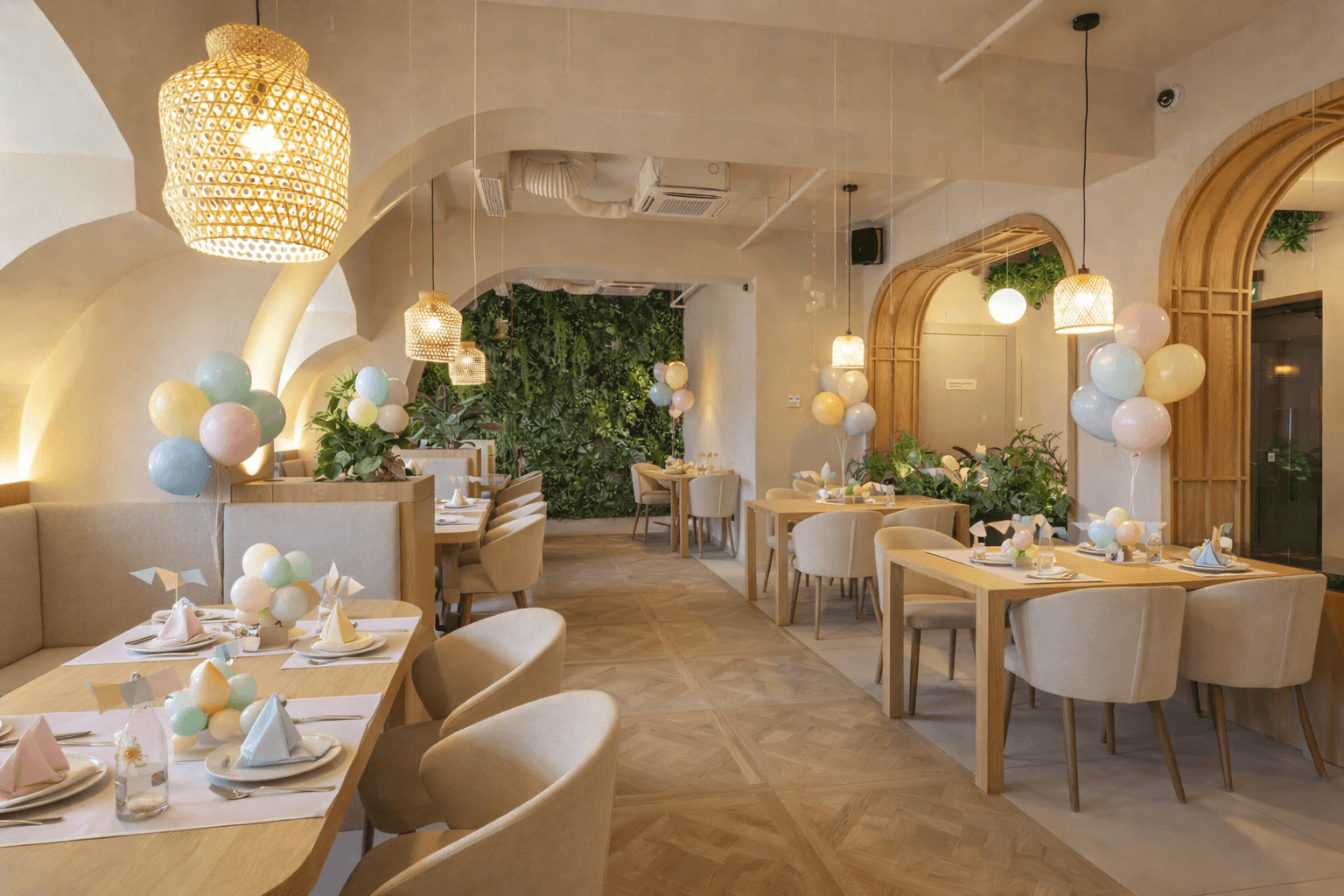 Bright restaurant interior decorated with pastel balloons, light wood tables, and woven pendant lights.