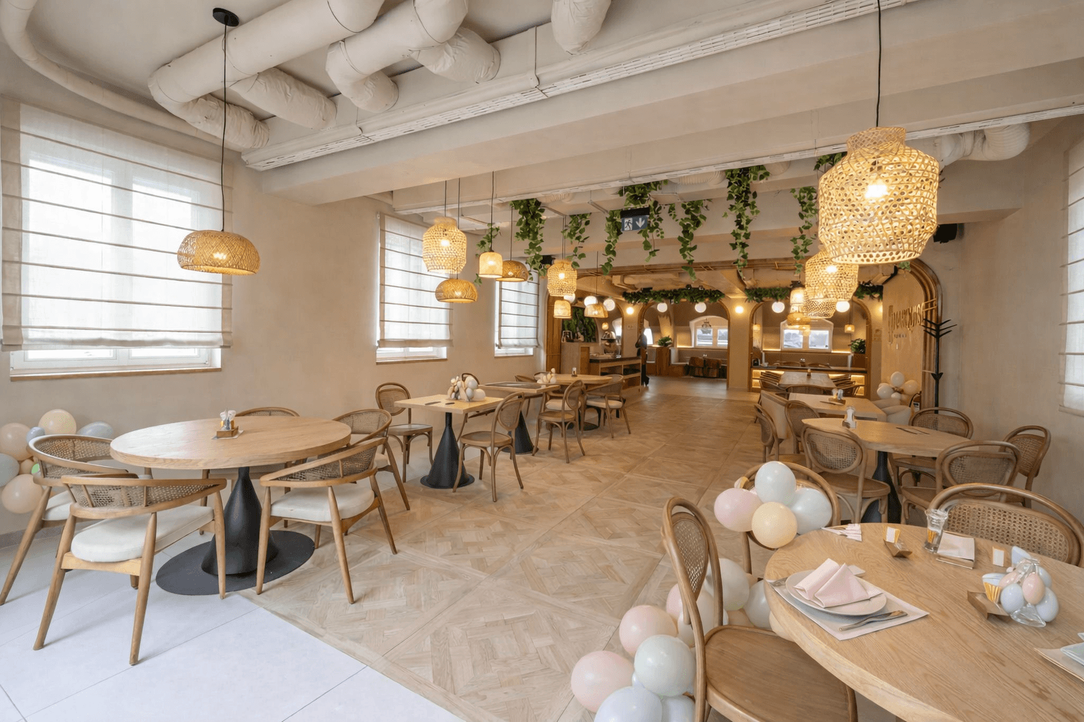 Bright restaurant interior with wooden tables, woven pendant lights, and festive pastel balloons.