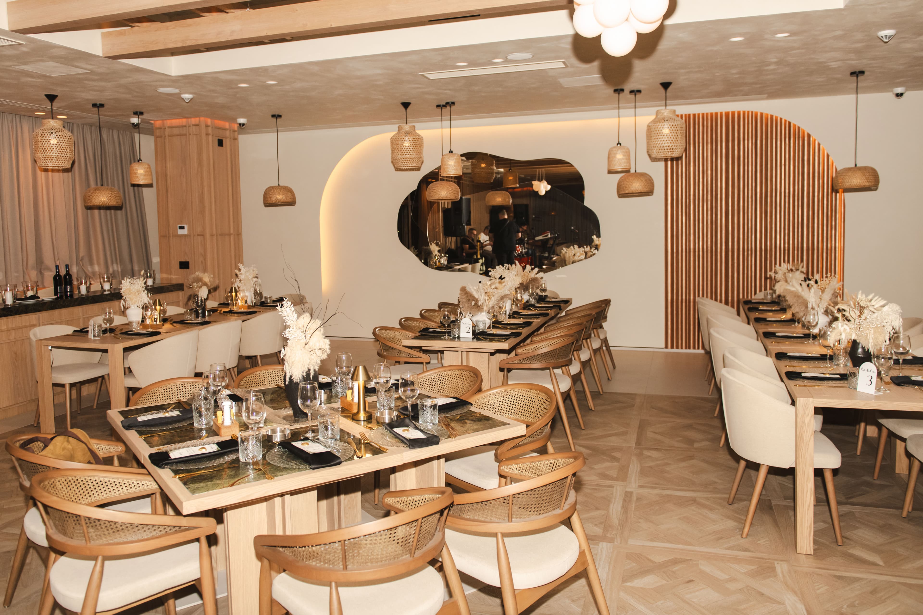 Elegant restaurant dining room with wooden tables, woven pendant lights, and dried floral centerpieces.