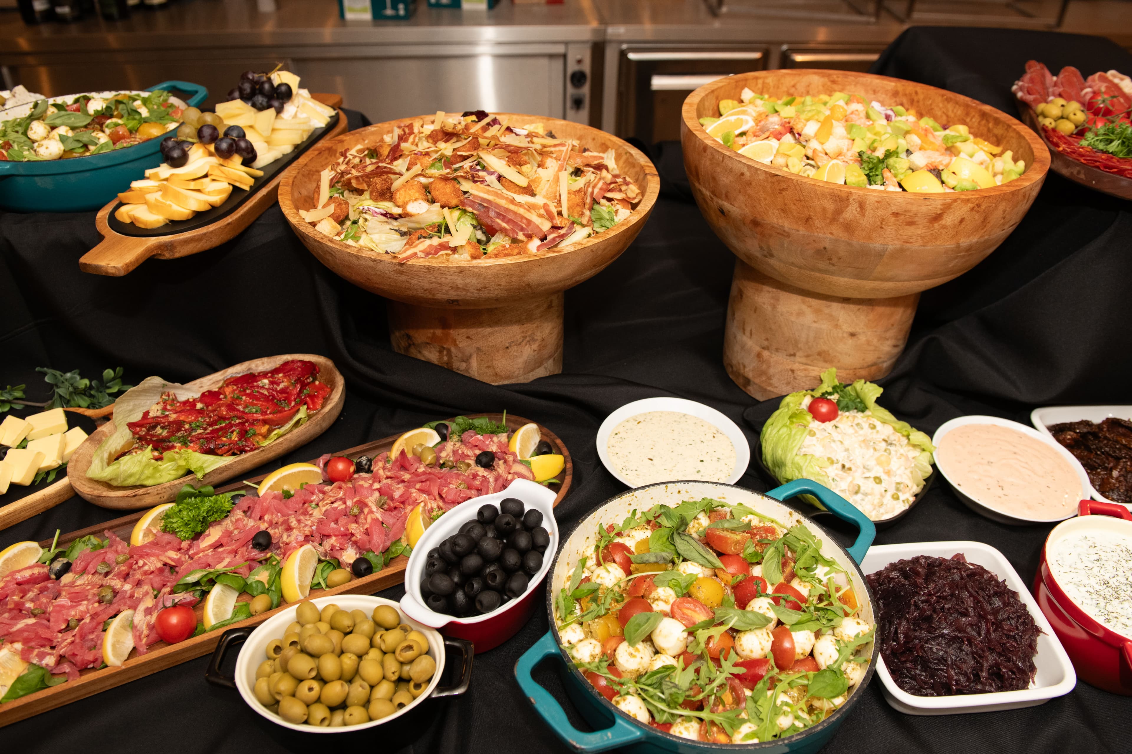 Lavish buffet spread featuring salads in wooden bowls, meat carpaccio, olives, and colorful appetizers.