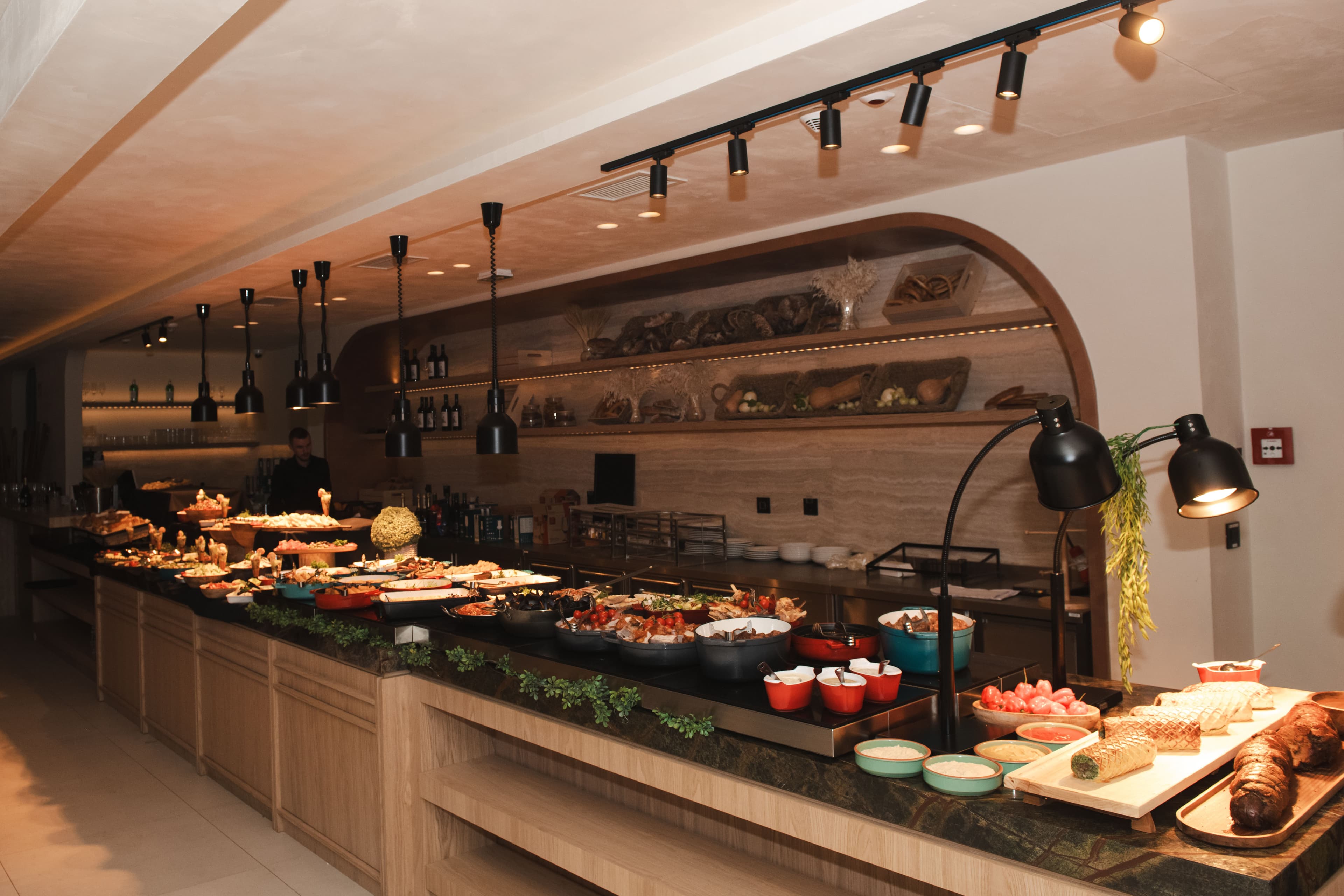 A long restaurant buffet counter showcasing a variety of dishes under warm, modern pendant lighting.