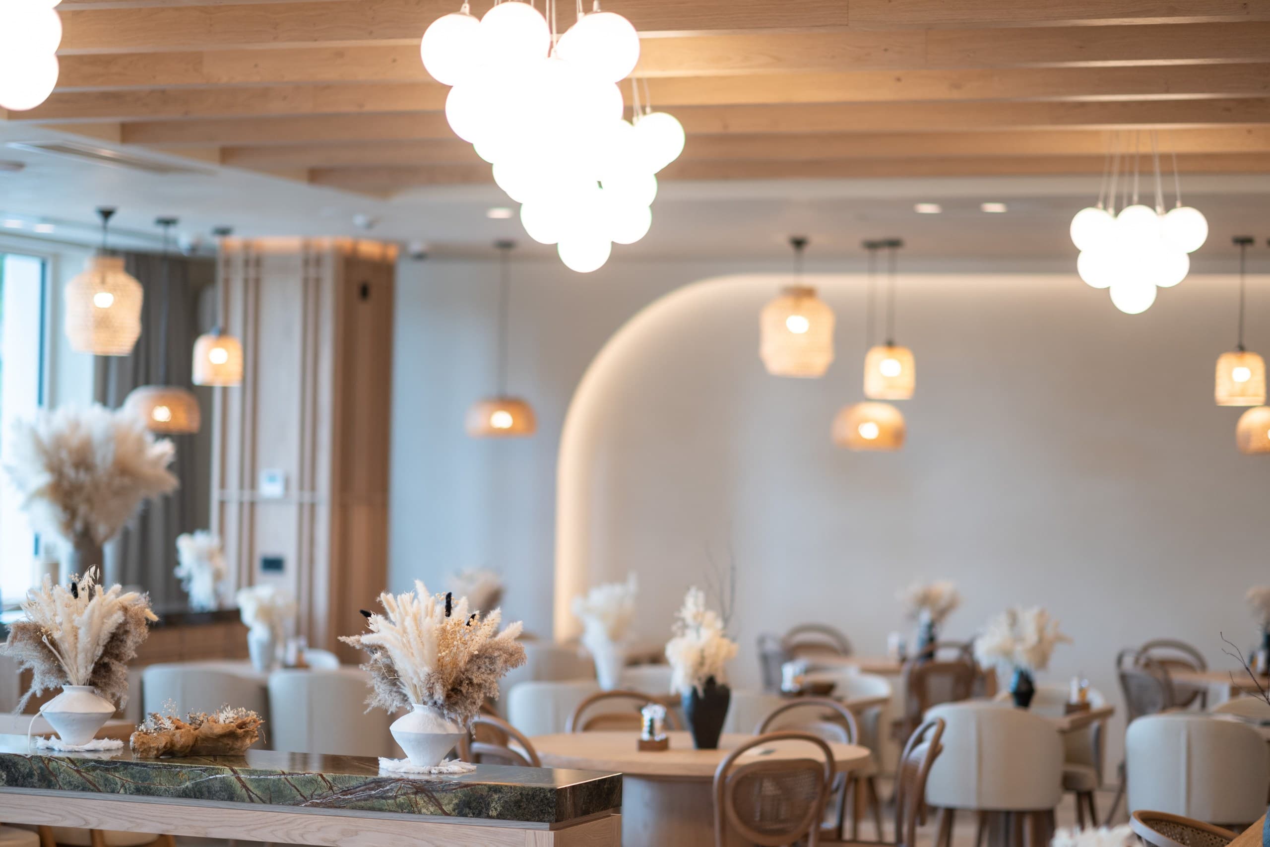 Modern restaurant interior featuring warm lighting, wooden tables, and decorative dried pampas grass.