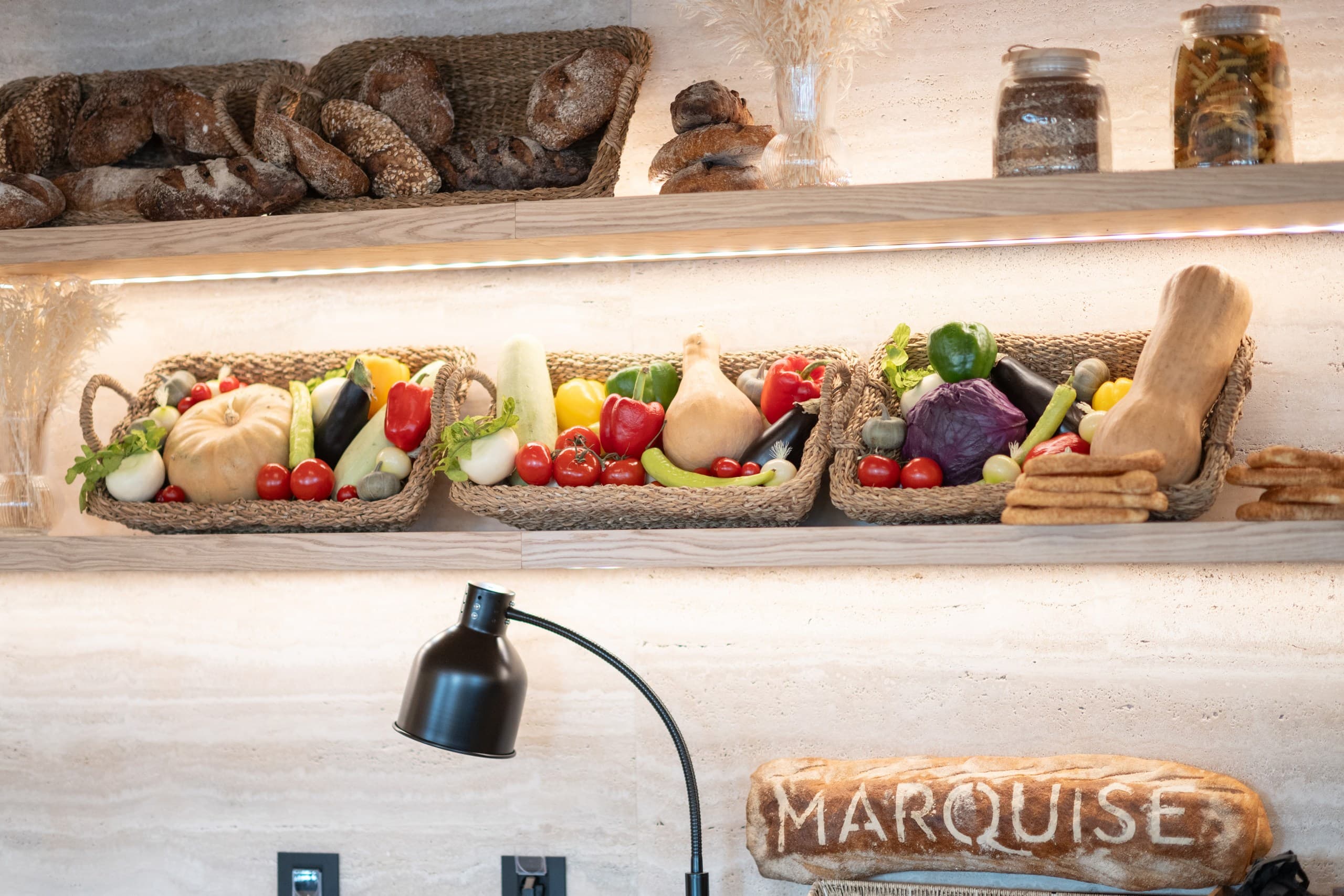 Artisan bread and baskets of fresh vegetables displayed on wooden shelves under warm lighting.