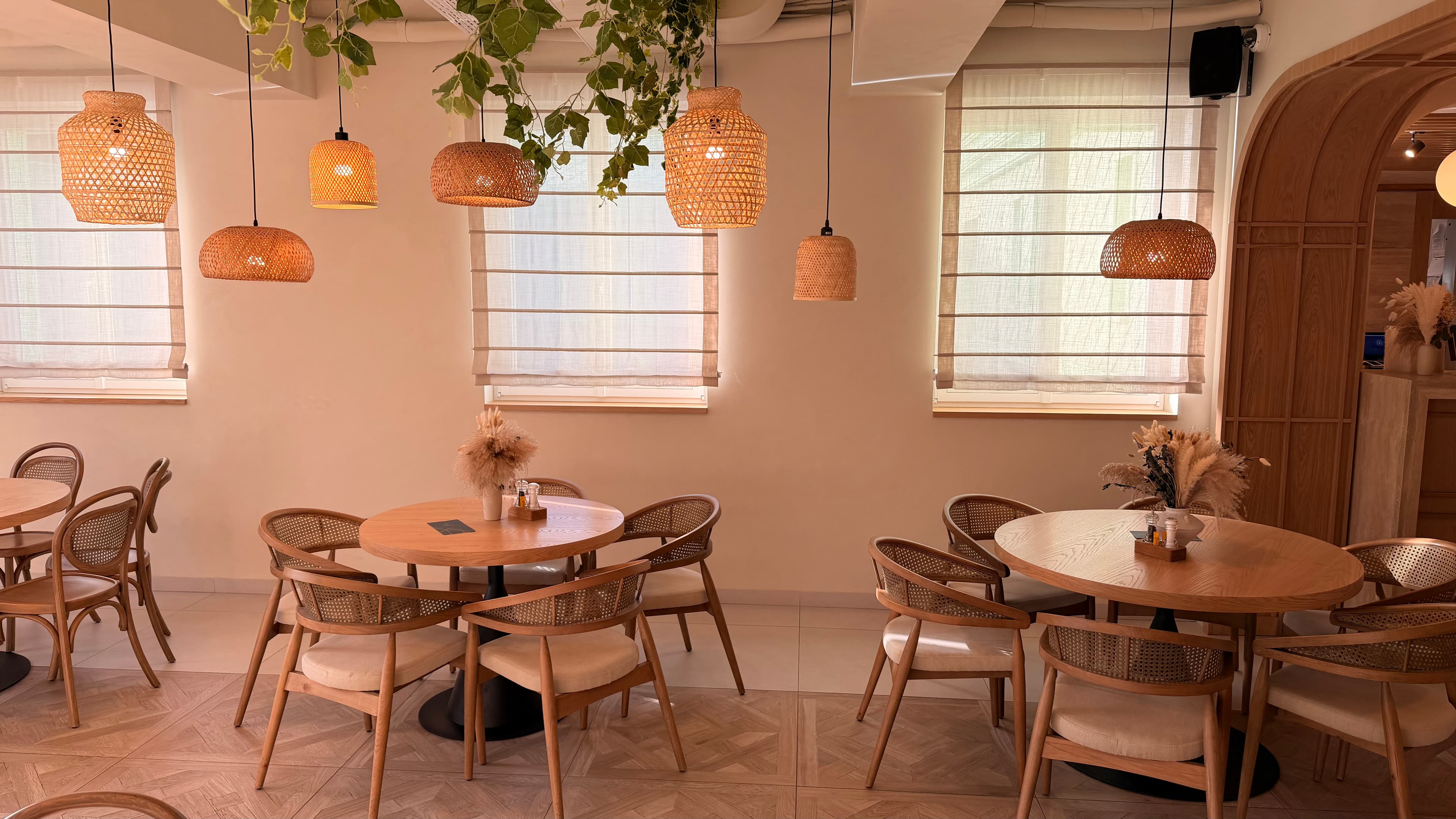 Cozy cafe interior featuring round wooden tables, rattan chairs, and hanging wicker pendant lights.