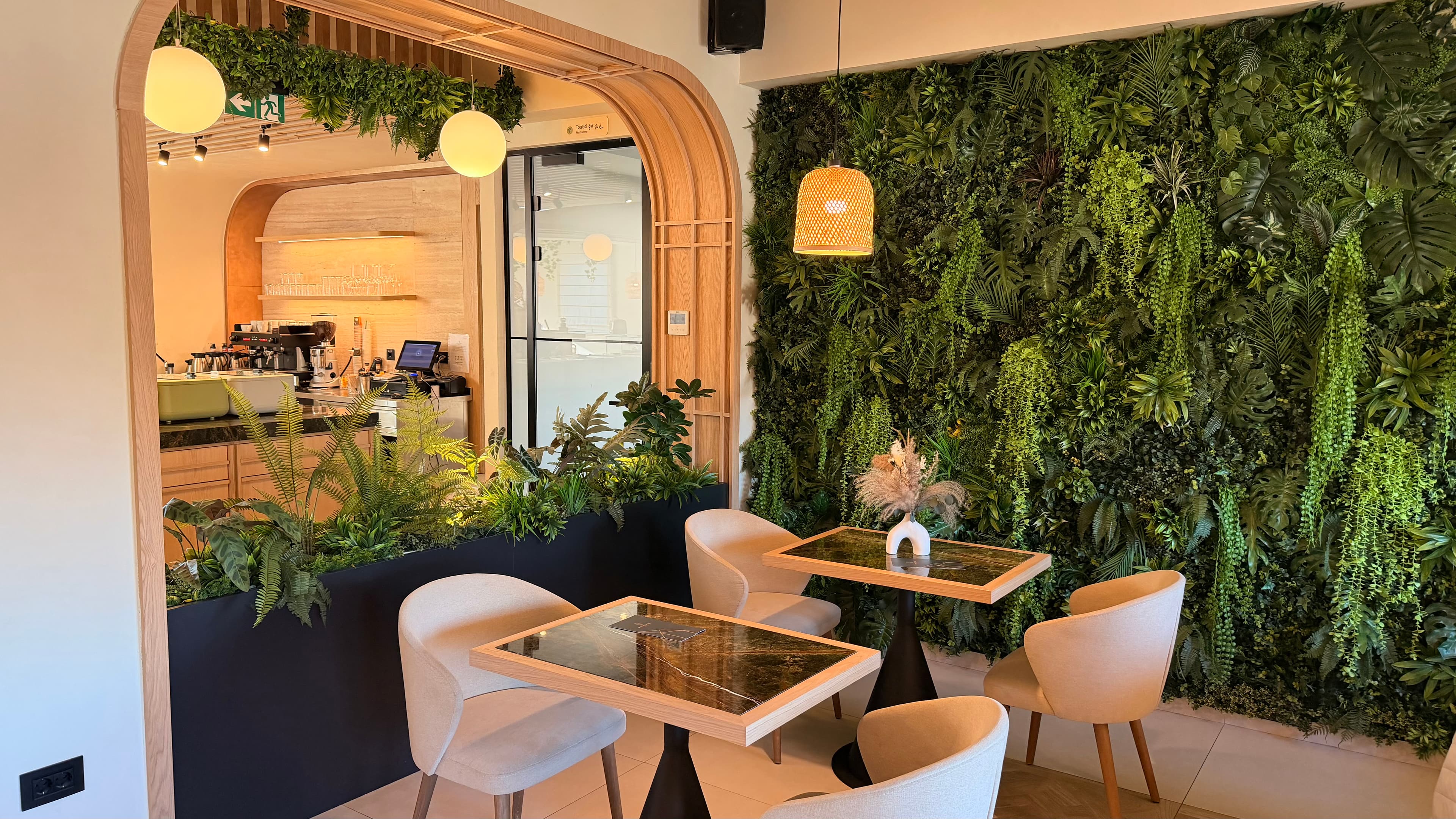Modern cafe seating area with marble tables, beige chairs, and a lush vertical garden wall.