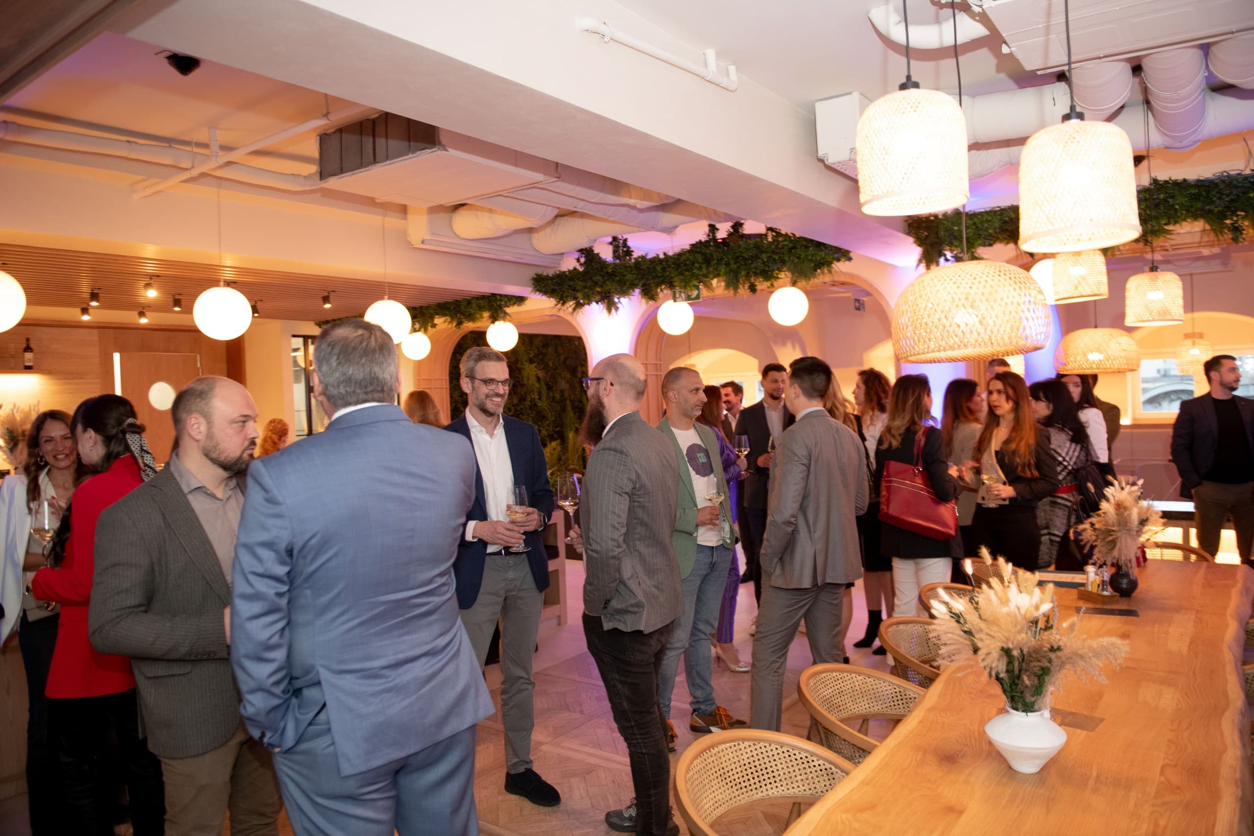 Professionals in business attire socialize and network at an indoor event with warm ambient lighting.
