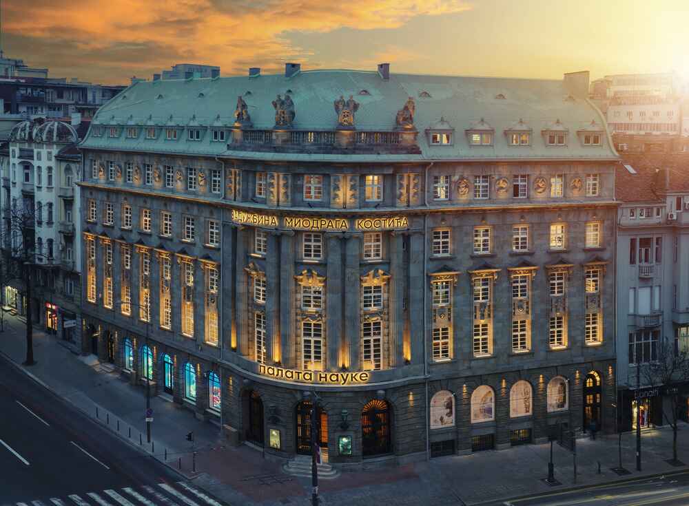 Ornate neoclassical building with illuminated windows and Cyrillic signage under a golden sunset sky.