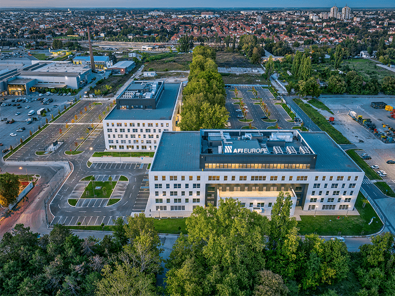 Aerial view of modern white office buildings and parking lots surrounded by lush green trees.